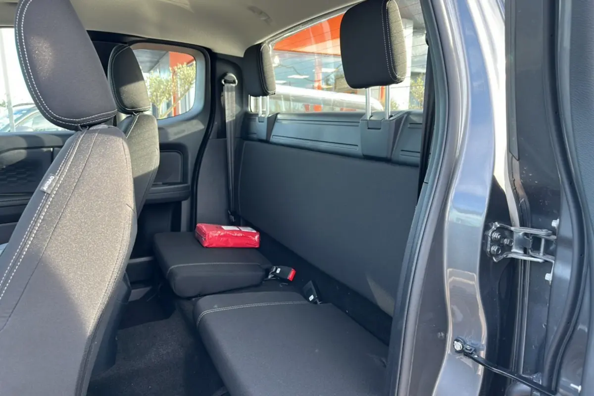 Vue intérieure arrière côté droit du Ford Ranger gris carbone, montrant les sièges SuperCab et un rideau coulissant fermé.