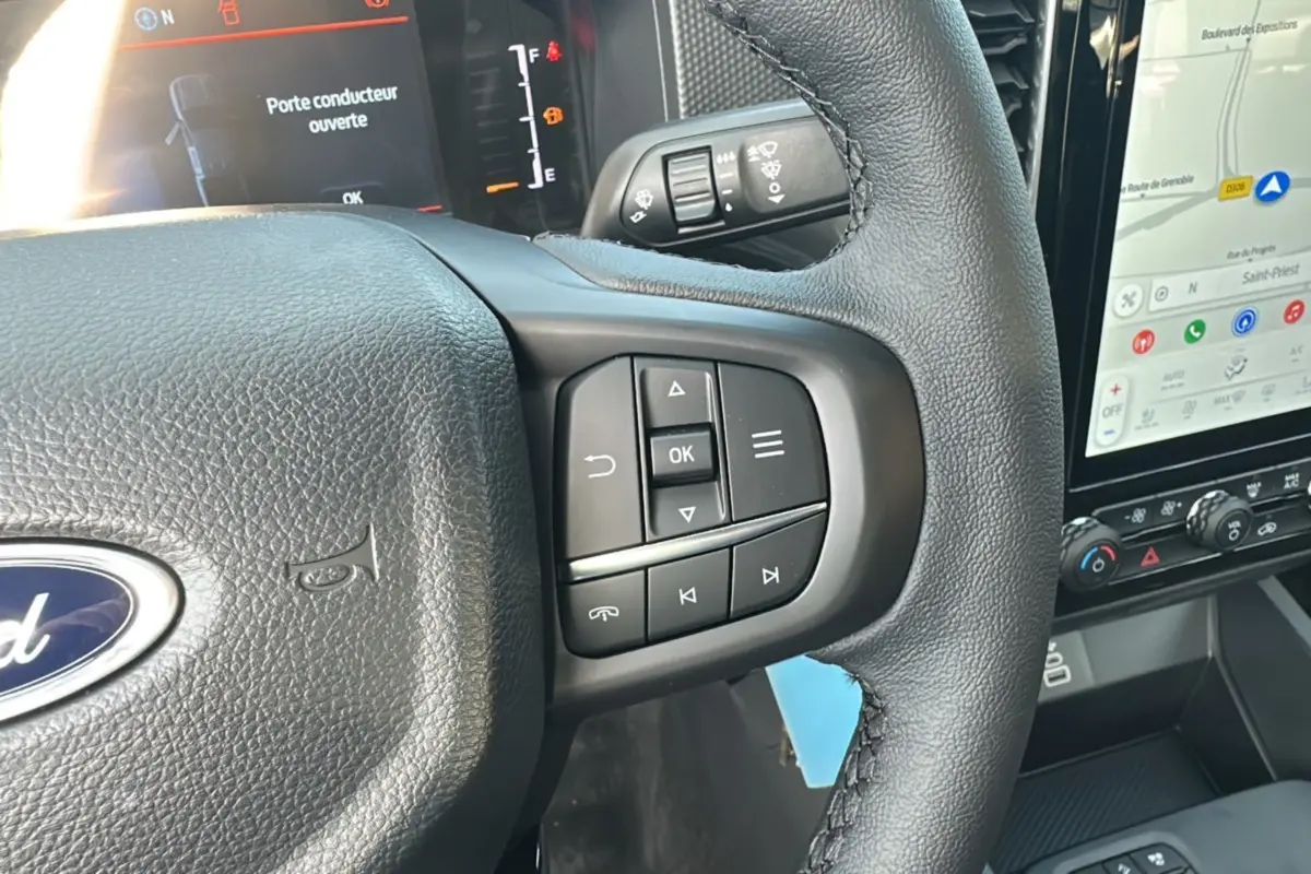 Gros plan sur le volant cuir multifonctions du Ford Ranger gris carbone, avec écran tactile et commandes au volant visibles.
