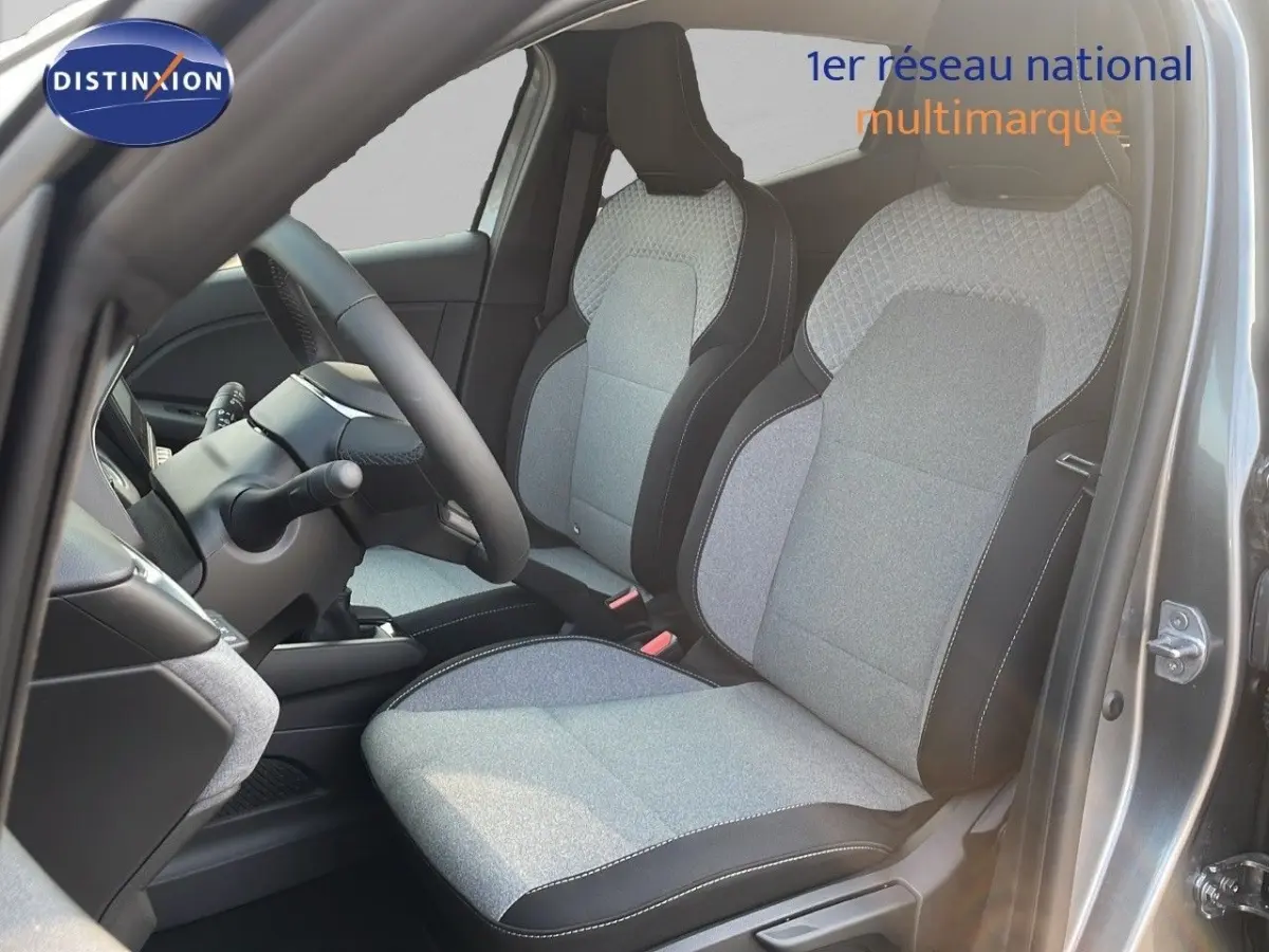 Vue intérieure côté conducteur de la Renault Clio 2025 avec sièges tissu gris clair et noir, volant multifonctions cuir synthétique.