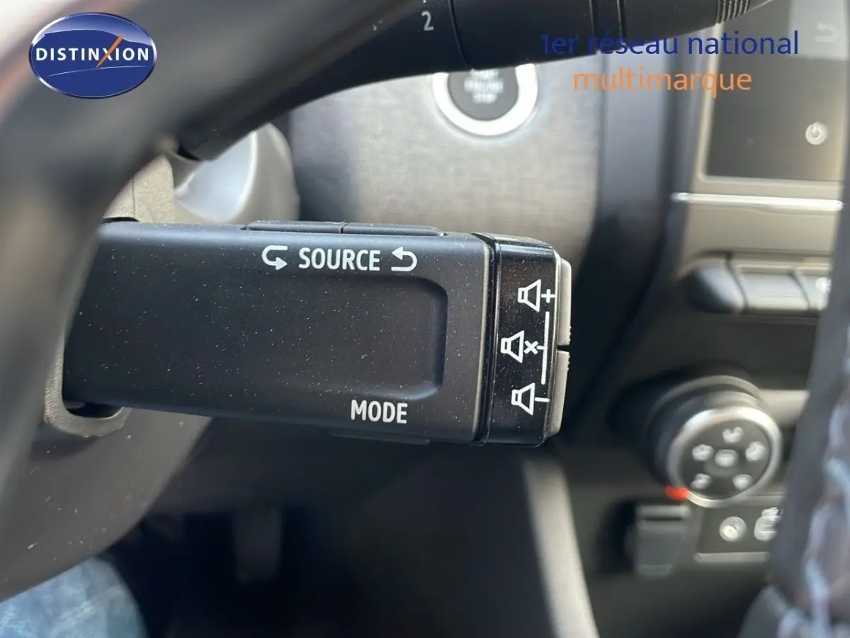 Gros plan sur la commande au volant gauche de la Renault Clio Evolution Blue dCi 100, avec boutons source et mode visibles.