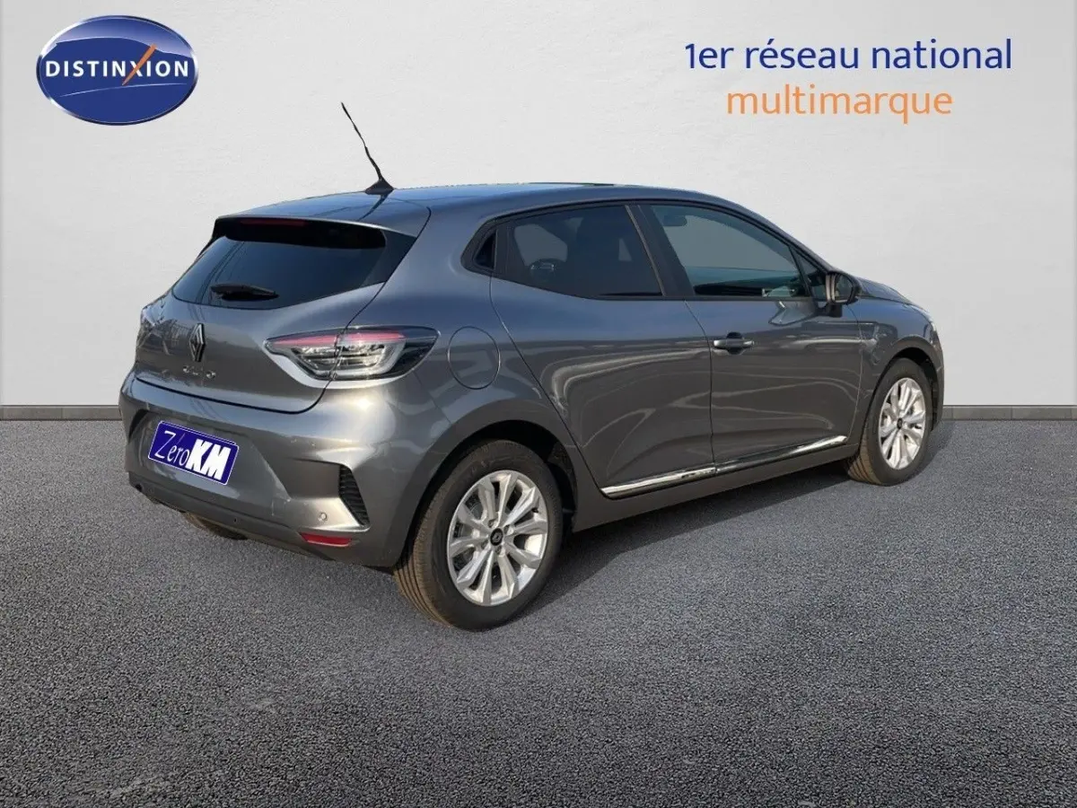 Vue 3/4 arrière droite d'une Renault Clio gris métallisé garée devant un mur blanc avec logo Distinxion.