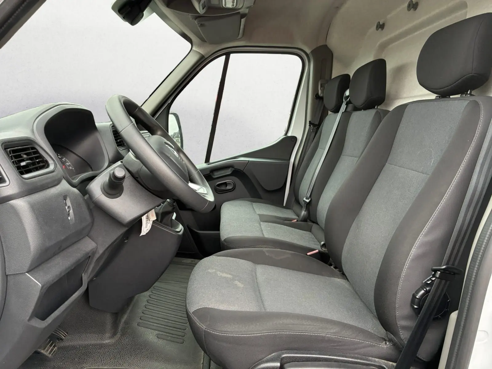Vue intérieure côté conducteur du Renault Master 2024 blanc, montrant les trois sièges avant gris et le tableau de bord simple.