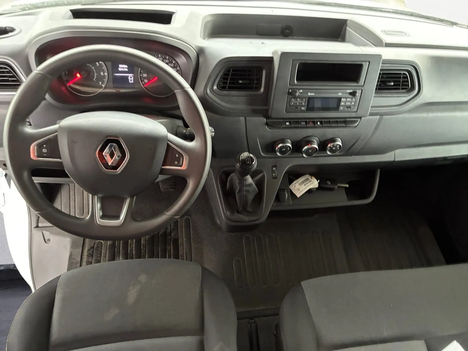 Vue intérieure du tableau de bord et volant du Renault Master blanc 2024, avec boîte manuelle et commandes centrales visibles.