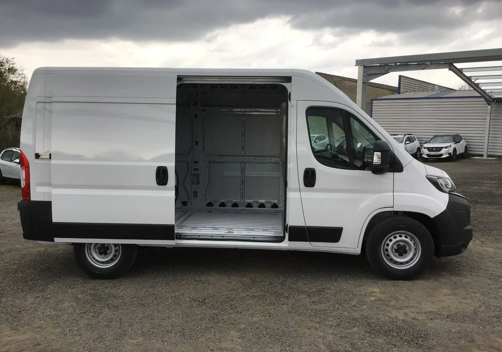Peugeot Boxer blanc vu de profil gauche avec porte coulissante ouverte montrant l'espace de chargement vide.