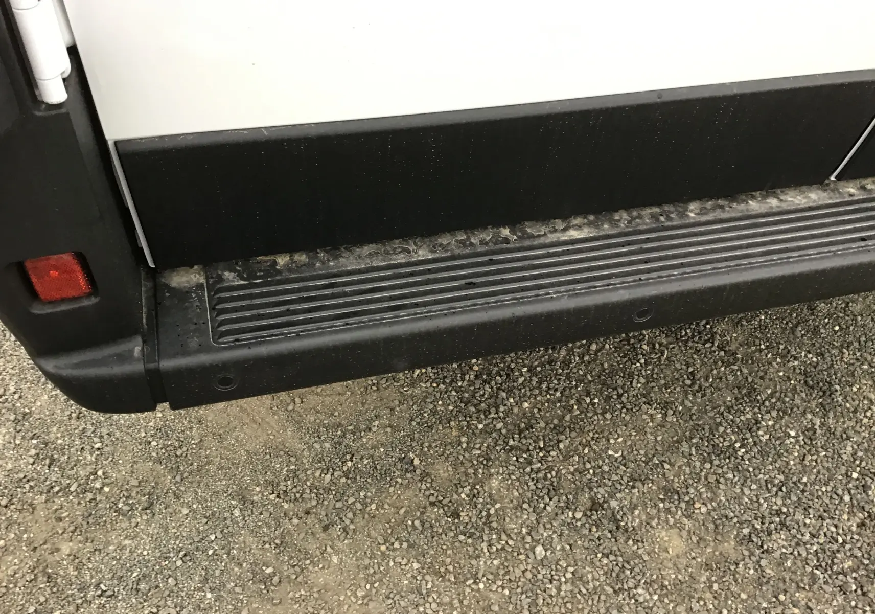 Gros plan sur la marche latérale noire du Peugeot Boxer Fourgon blanc, côté gauche, avec traces de boue.