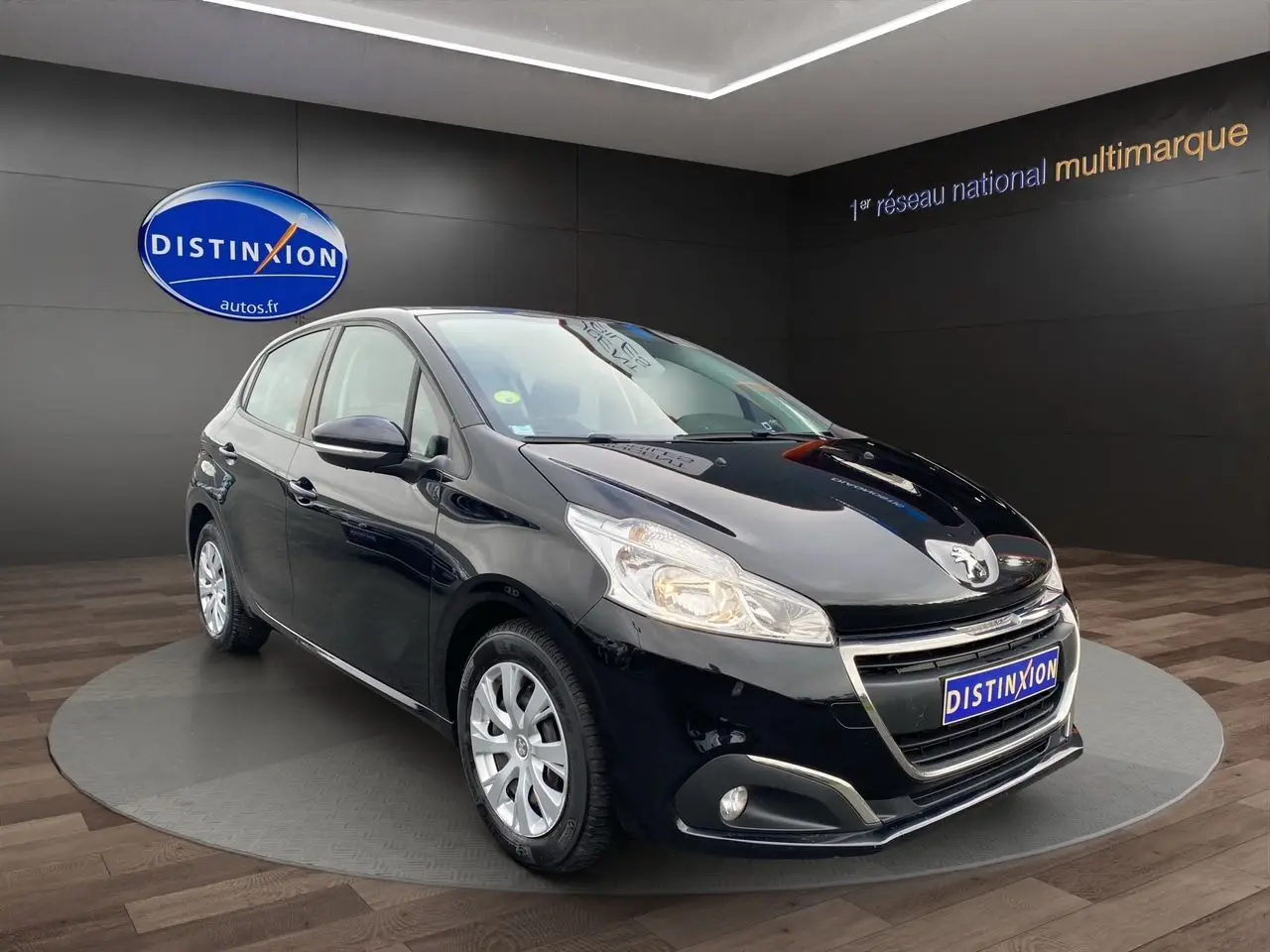 Peugeot 208 Affaire noir vue 3/4 avant droit en intérieur, avec phares allumés et jantes argentées.