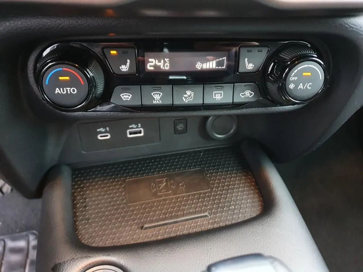 Gros plan sur la console centrale du Nissan Juke 2025, montrant la climatisation automatique et le chargeur sans fil.