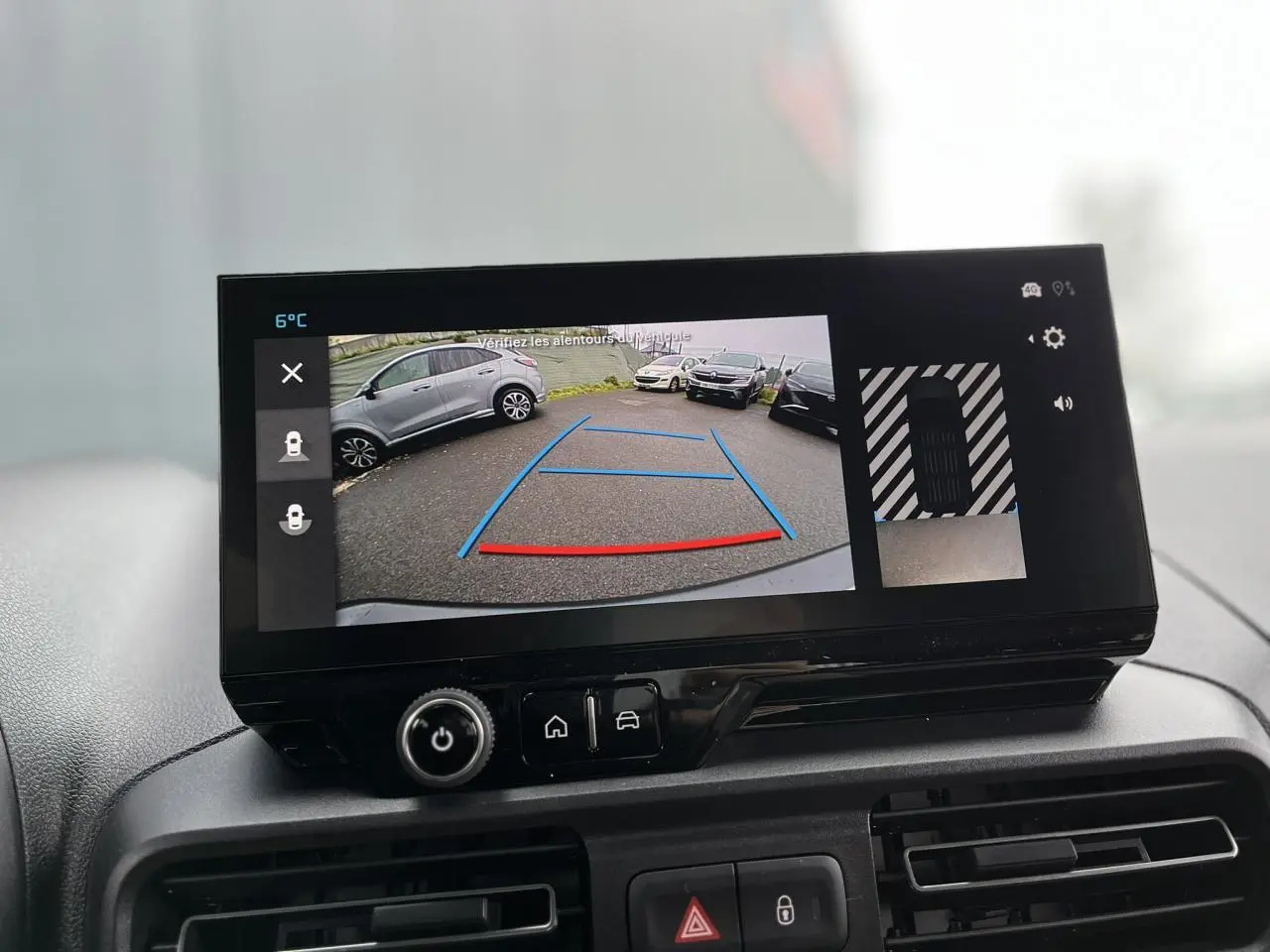 Écran tactile intérieur montrant la caméra de recul avec vue arrière sur parking et véhicules environnants.