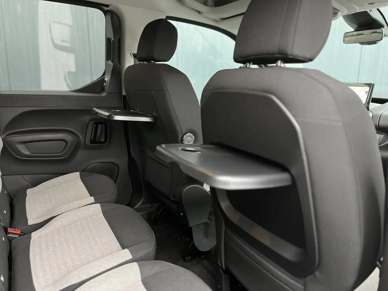 Vue intérieure arrière droite du Citroën Berlingo Multispace 2025, sièges gris avec tablettes rabattables noires.