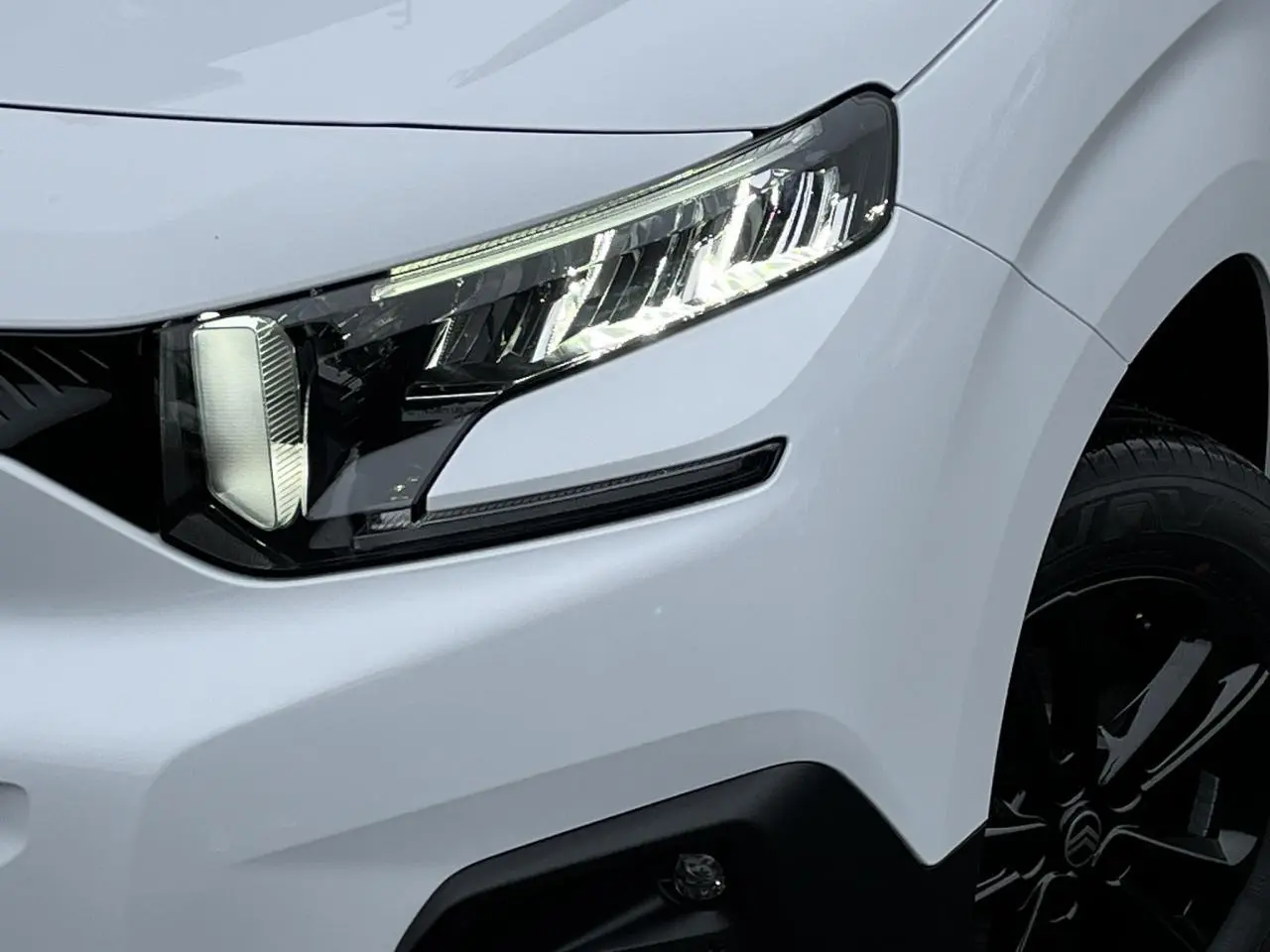Gros plan sur le phare avant droit et la jante alliage noire du Citroën Berlingo Multispace blanc Glacier 2025.