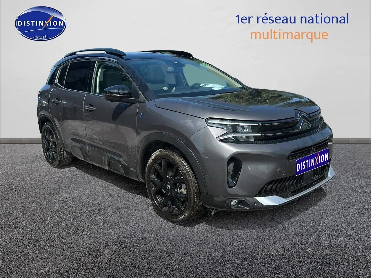Vue 3/4 avant droit du Citroën C5 Aircross gris platinium avec jantes noires et barres de toit visibles.