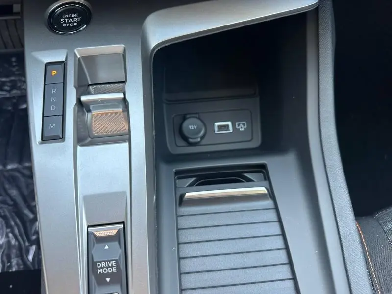 Gros plan sur la console centrale intérieure de la Peugeot 308 bleu, montrant la boîte auto, bouton start/stop et prises USB et 12V.