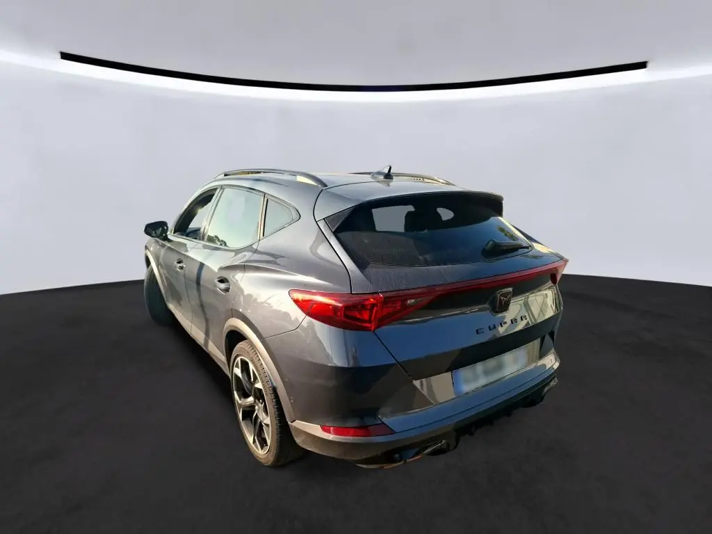Vue 3/4 arrière droite d'une CUPRA Formentor gris foncé 2023 avec feux arrière reliés et toit ouvrant.