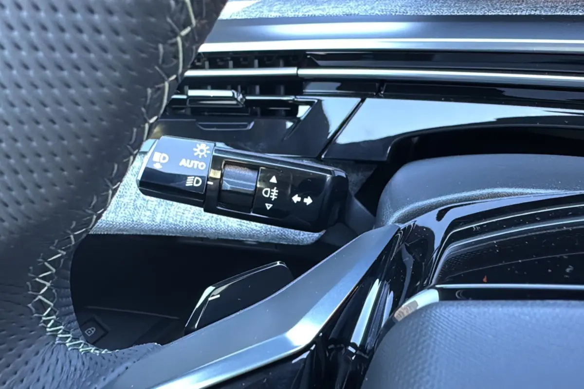 Gros plan sur la manette des feux et clignotants côté gauche du volant cuir du Peugeot 3008 Hybrid blanc toit noir.