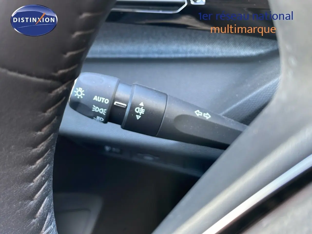 Gros plan sur la manette de clignotant et feux, à gauche du volant en cuir noir du Peugeot 308 SW gris Artense.