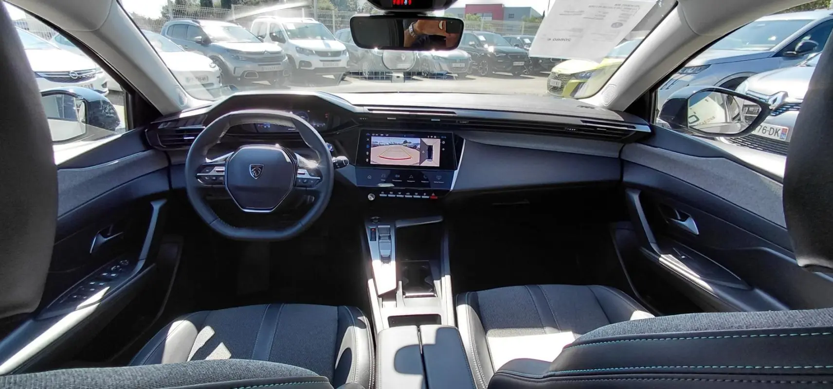 Vue intérieure avant de la Peugeot 308 Hybrid 145 gris, avec volant compact et écran tactile affichant la caméra de recul.
