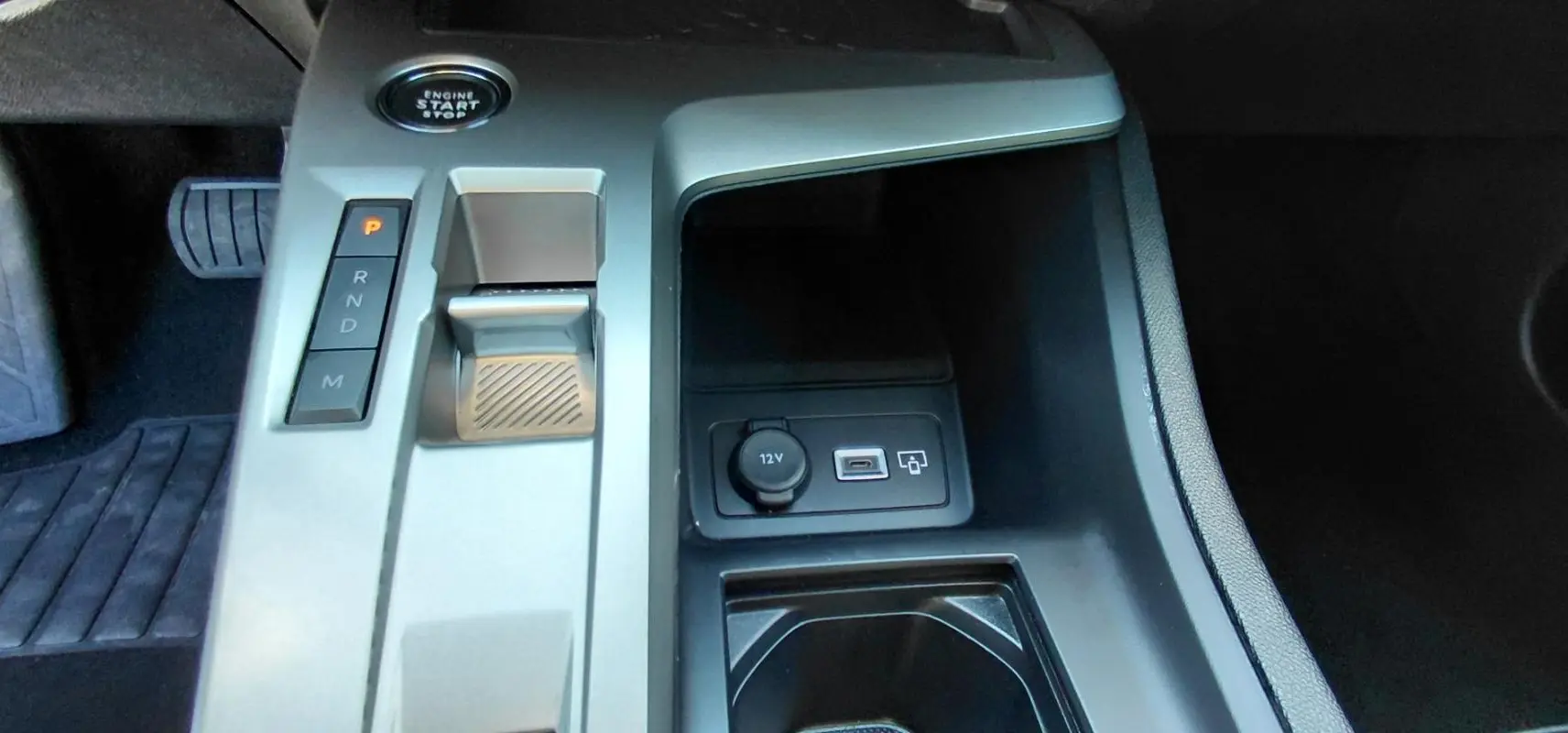 Vue rapprochée de la console centrale grise du Peugeot 308 Hybrid 145 e-DCS6 Allure avec bouton start, levier de vitesses et ports USB et 12V.