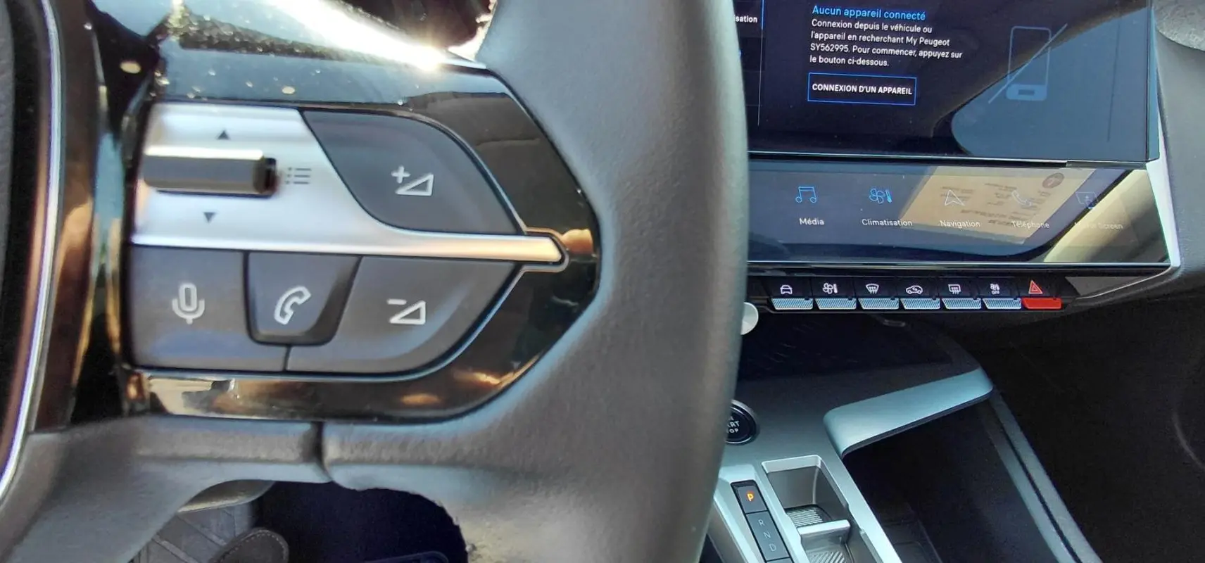 Gros plan sur le volant et la console centrale de la Peugeot 308 Hybrid 145 gris, montrant les commandes au volant et l’écran tactile.