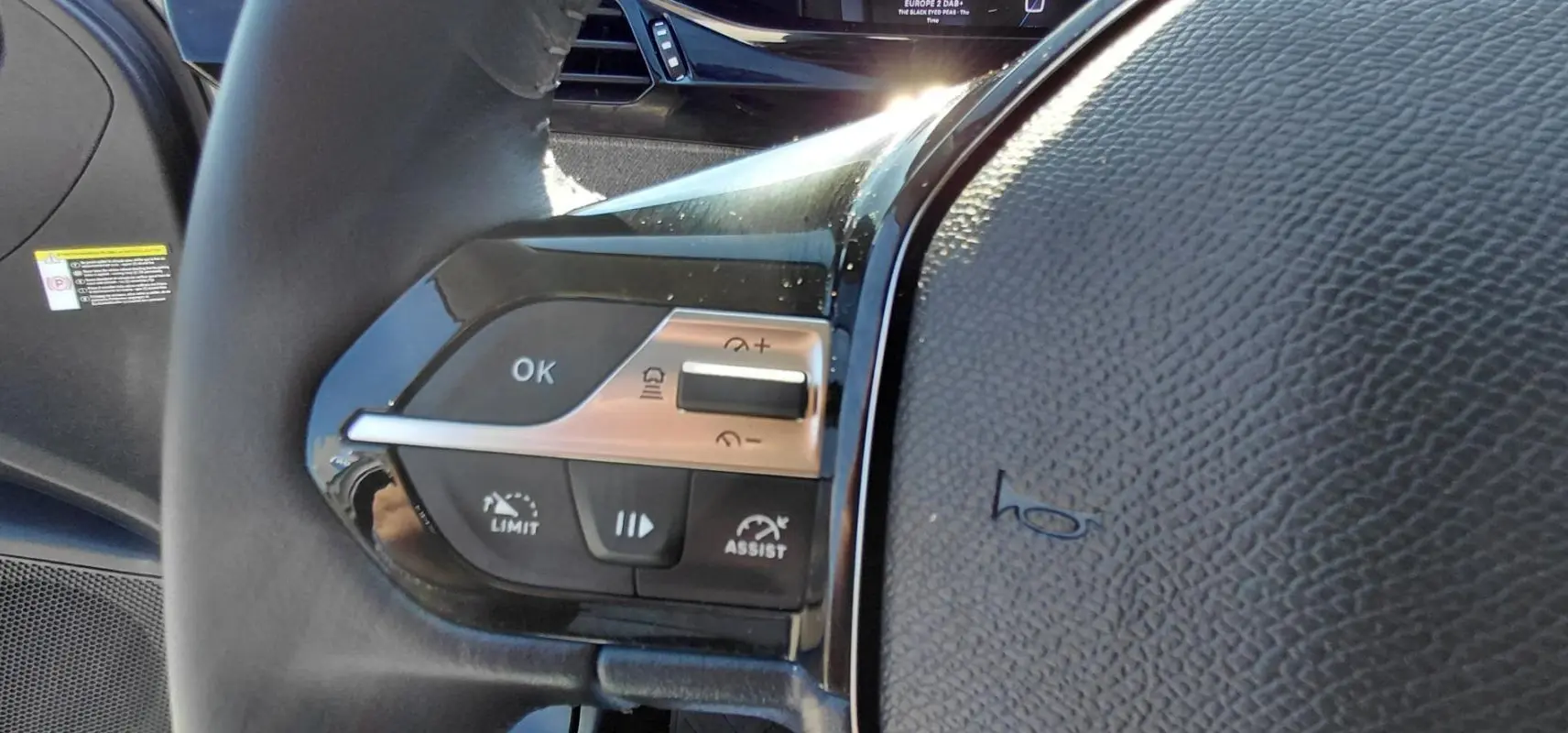 Détail du volant côté gauche du Peugeot 308 Hybrid gris, montrant les commandes de régulateur et limiteur de vitesse.