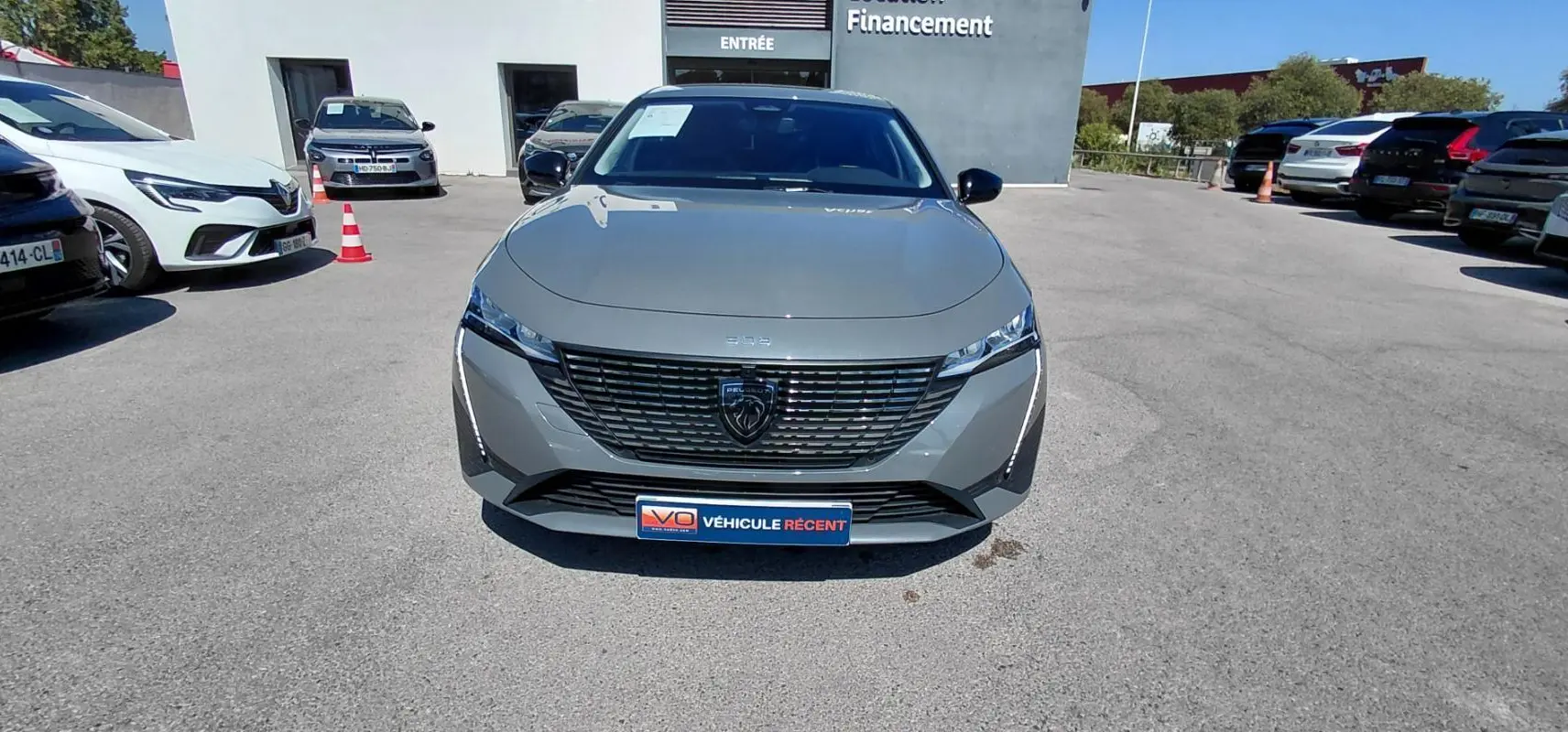 Vue avant d'une Peugeot 308 Hybrid 145 gris métallisé avec calandre noire et feux LED fins, stationnée en extérieur.