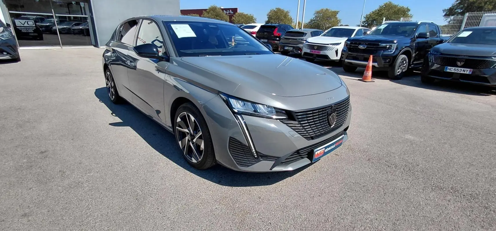 Peugeot 308 Hybrid gris vue 3/4 avant droit, avec jantes alliage et calandre au lion noir mat.