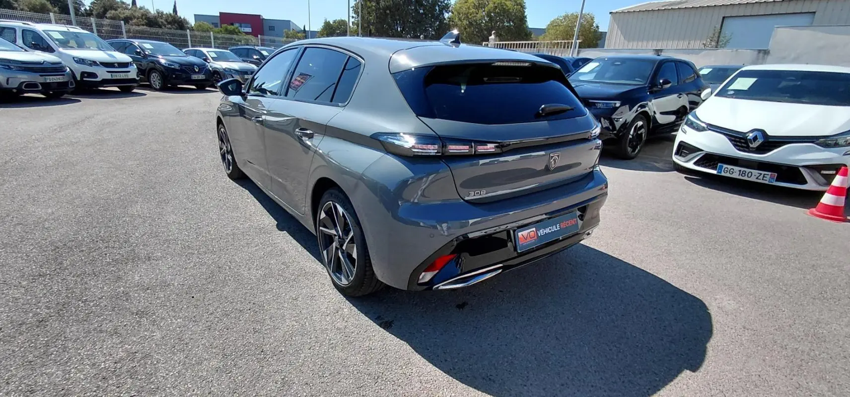Vue 3/4 arrière d'une Peugeot 308 Hybrid gris métallisé avec jantes alliage 17 pouces, stationnée en extérieur.