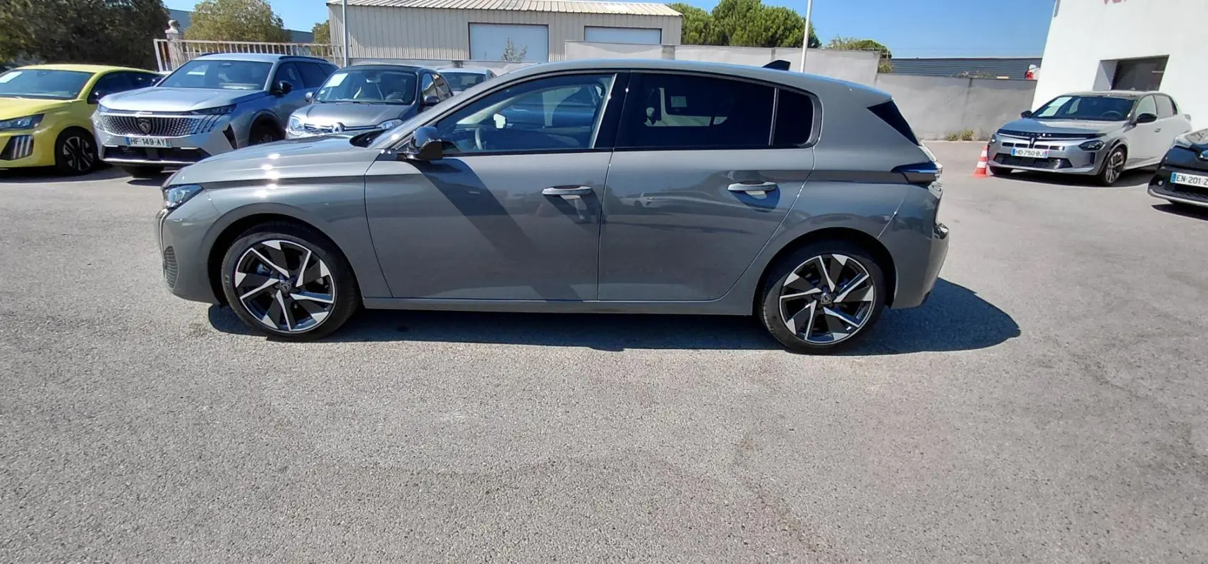 Profil côté gauche d'une Peugeot 308 gris métallisé avec jantes alliage 17 pouces, en extérieur sur parking.