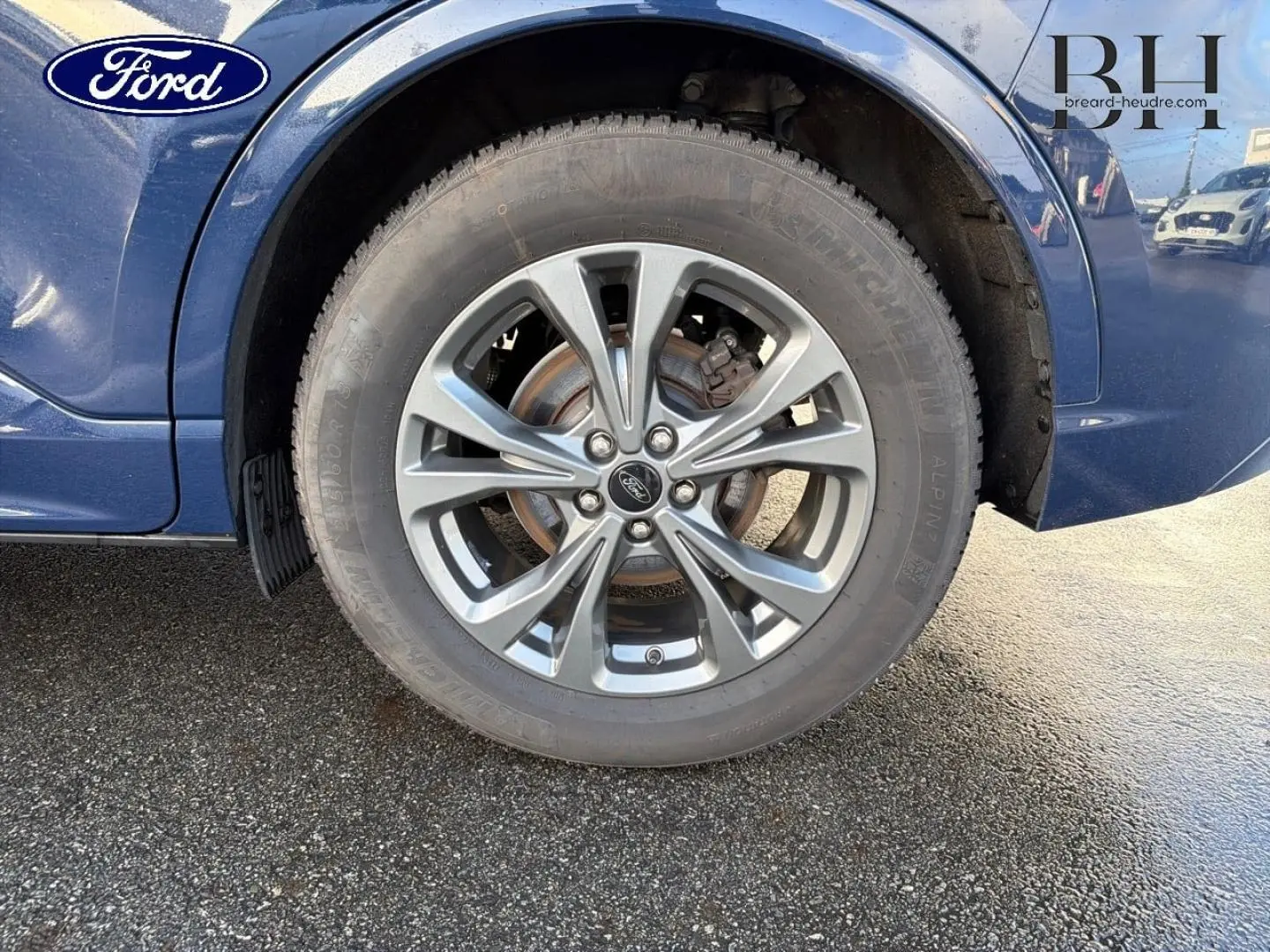 Gros plan sur la roue avant gauche et la jante alu grise d’un Ford Kuga bleu Abysse 2023.