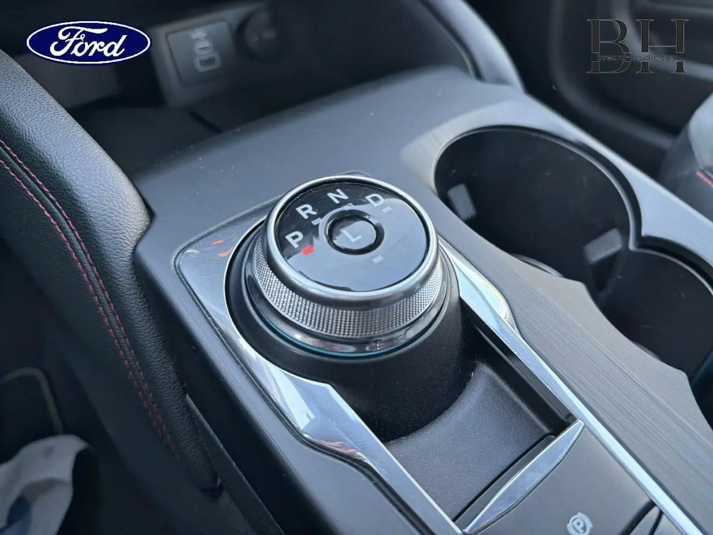 Gros plan sur la molette de boîte automatique du Ford Kuga 2023, avec console noire et surpiqûres rouges visibles.