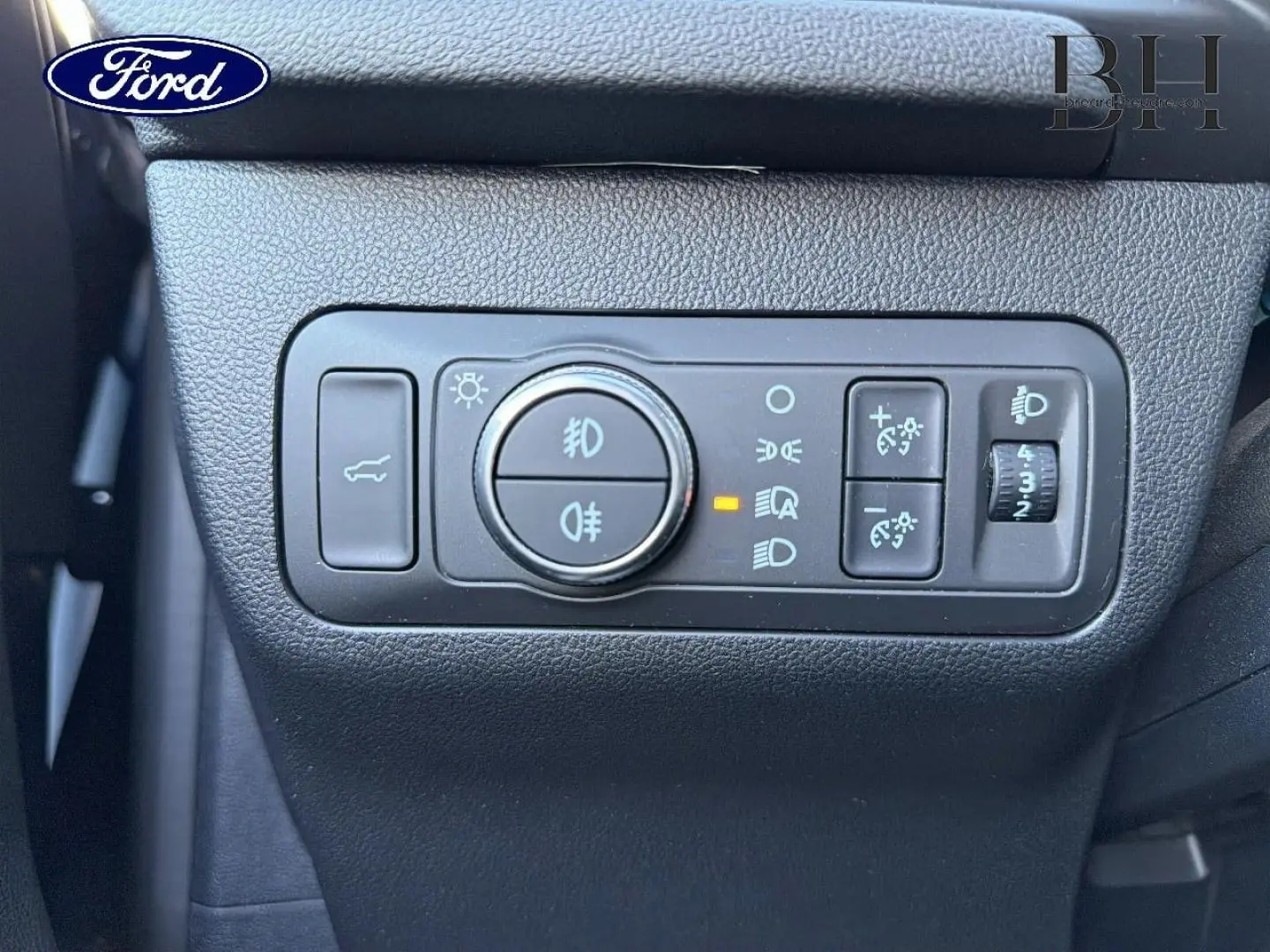 Gros plan sur les commandes d’éclairage et de réglage des phares du Ford Kuga 2023, tableau de bord noir.
