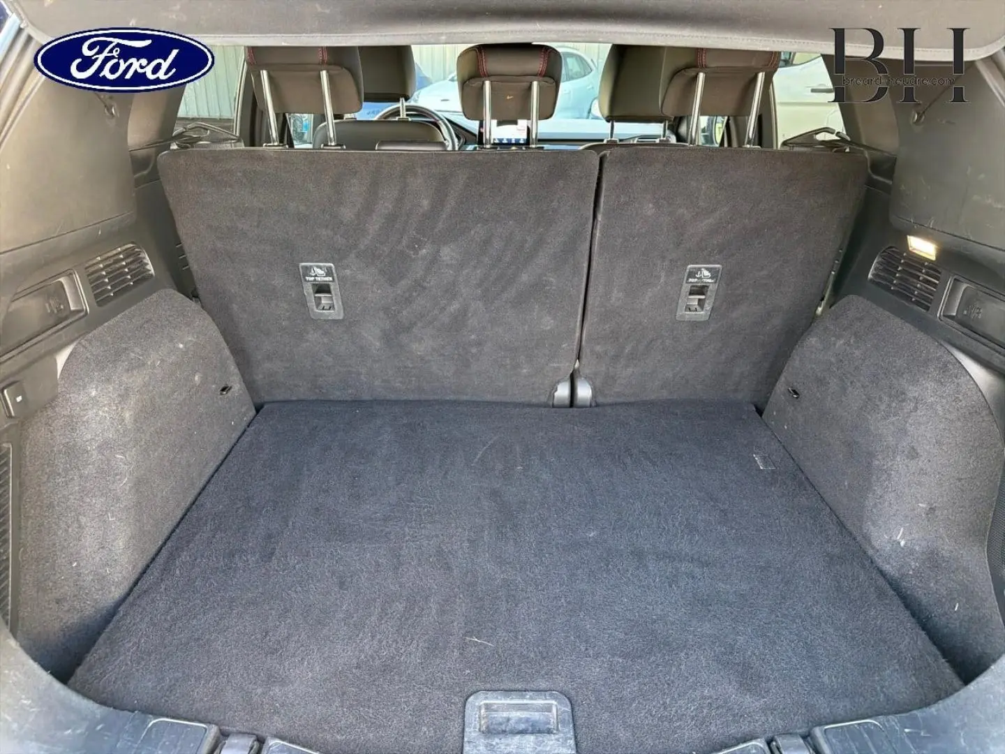 Coffre ouvert vu de l'arrière d'un Ford Kuga bleu, banquette arrière en tissu noir relevée.