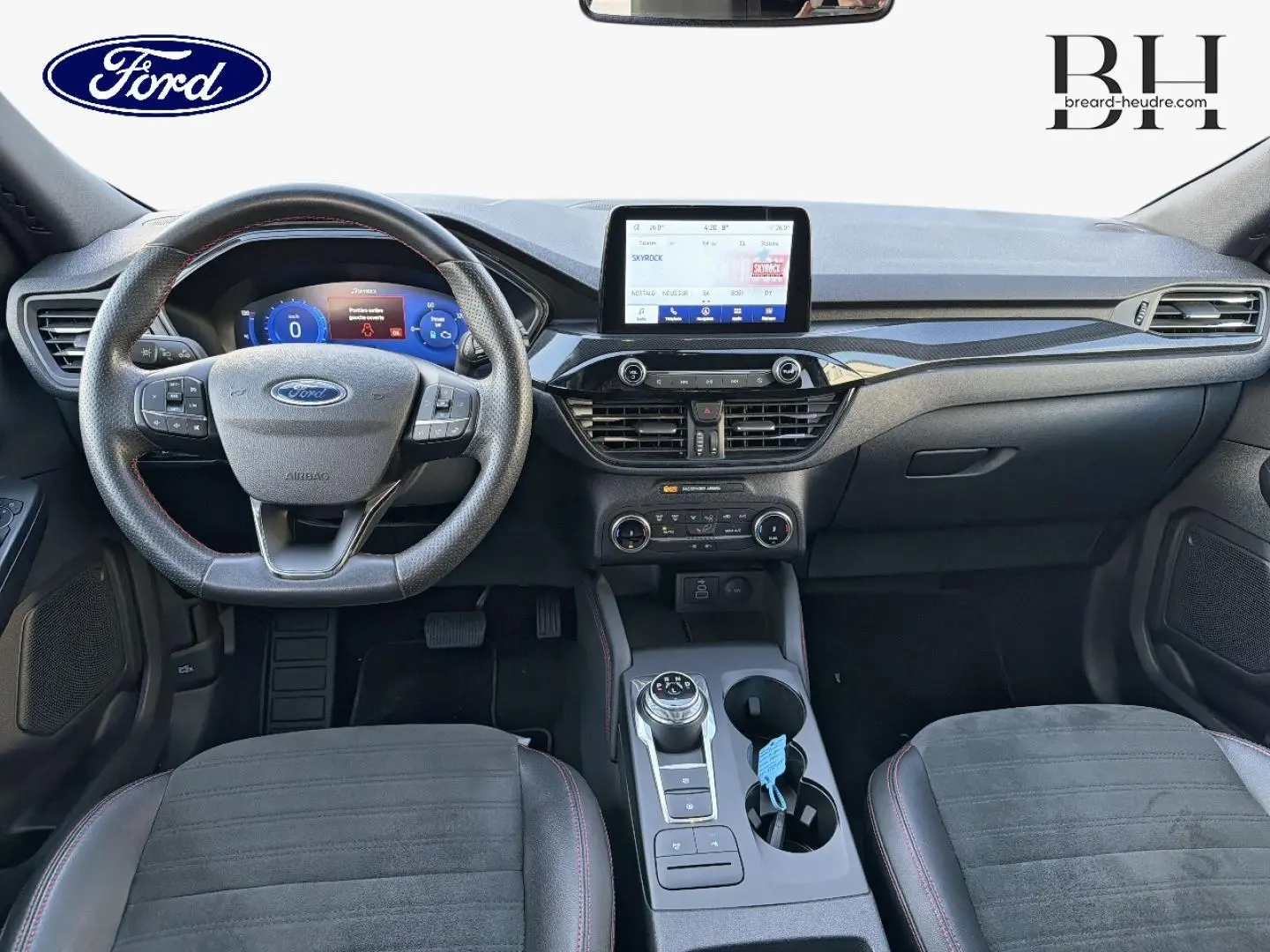 Vue intérieure avant du Ford Kuga 2023, tableau de bord noir avec écran tactile central et volant cuir multifonction.