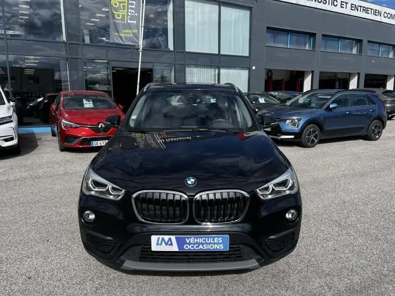 Vue avant d’un BMW X1 20D noir métal, avec calandre double haricot et phares LED visibles sur un parking extérieur.