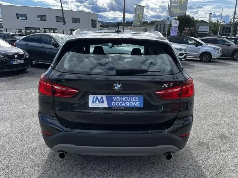 Vue arrière d'un BMW X1 noir métal 2017 avec logo et plaque "Véhicules Occasions" sur un parking extérieur.