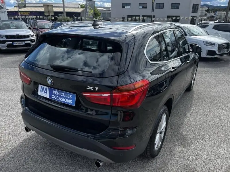 Vue 3/4 arrière droite d’un BMW X1 noir métal de 2017, avec feux arrière allongés et double sortie d’échappement visible.
