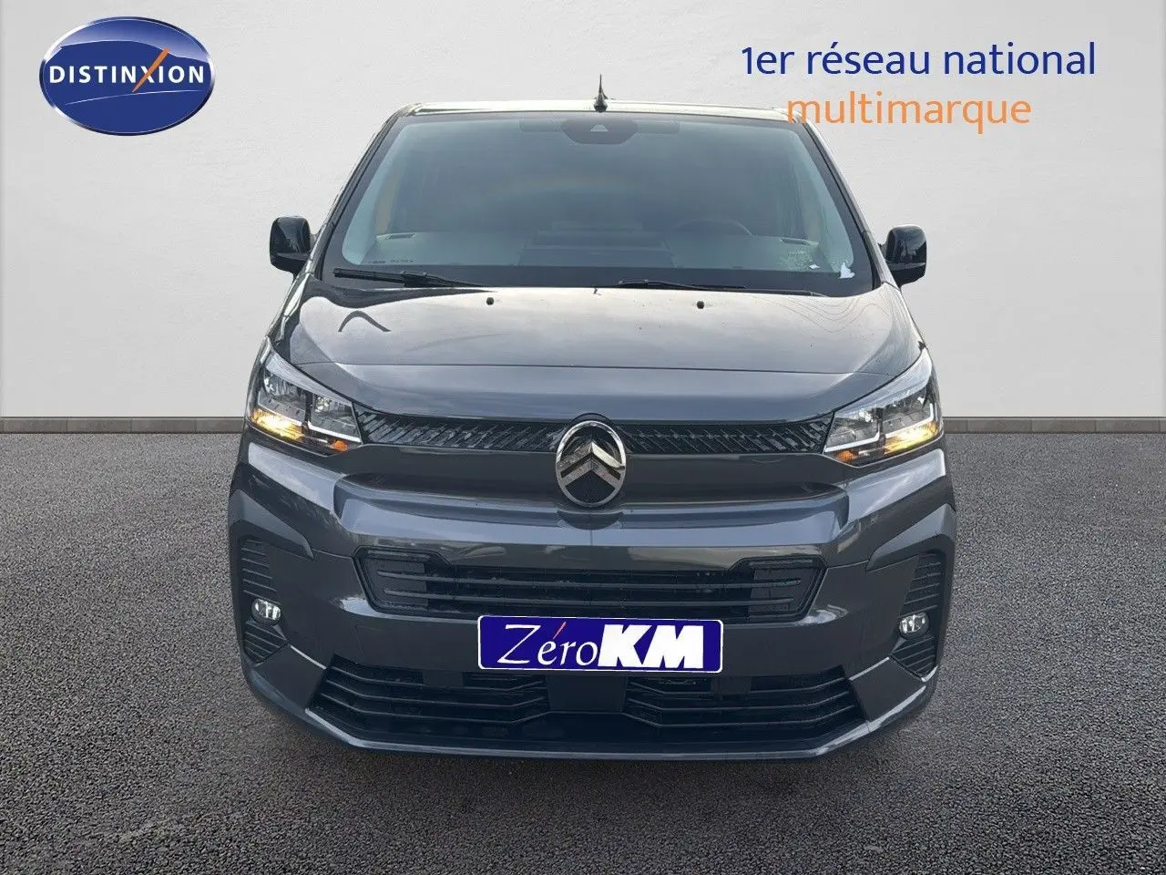 Vue frontale d'un Citroën Jumpy Fourgon XL gris titane métal avec feux allumés sur fond neutre.
