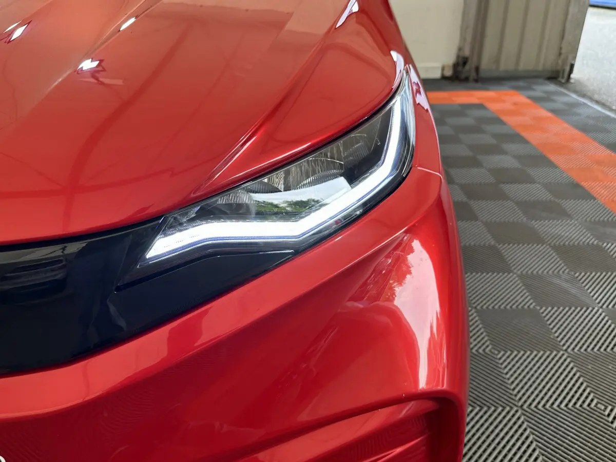 Gros plan sur le phare avant gauche d'une Aixam Ambition E City Pack rouge 2025 avec éclairage LED distinctif.