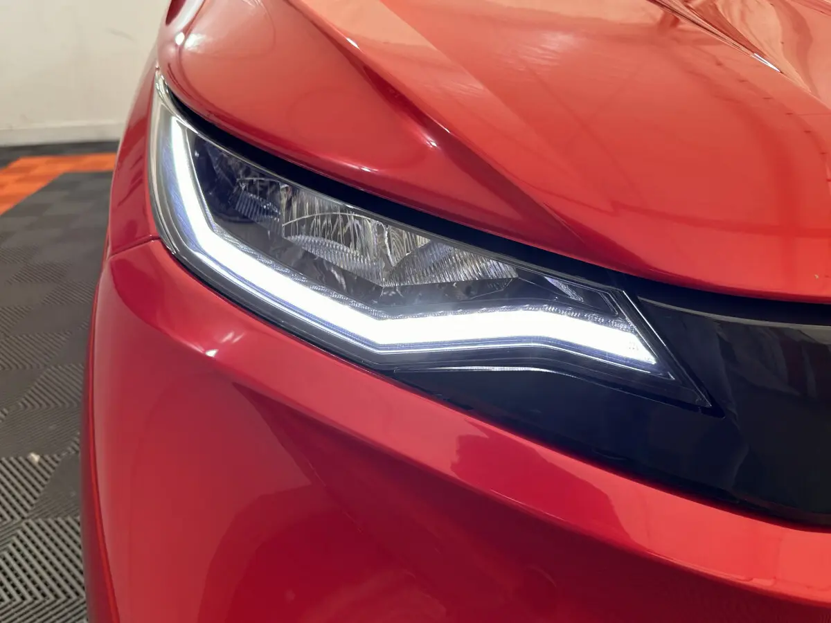 Gros plan sur le phare avant gauche lumineux d'une AIXAM AMBITION E CITY PACK rouge électrique 2025.