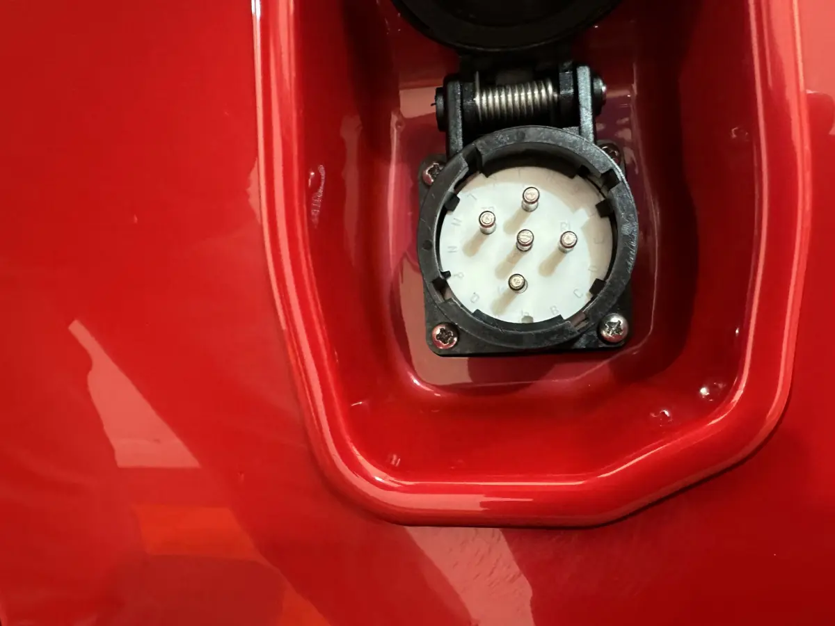 Prise de recharge électrique en gros plan sur la carrosserie rouge de l'AIXAM AMBITION E CITY PACK 2025.