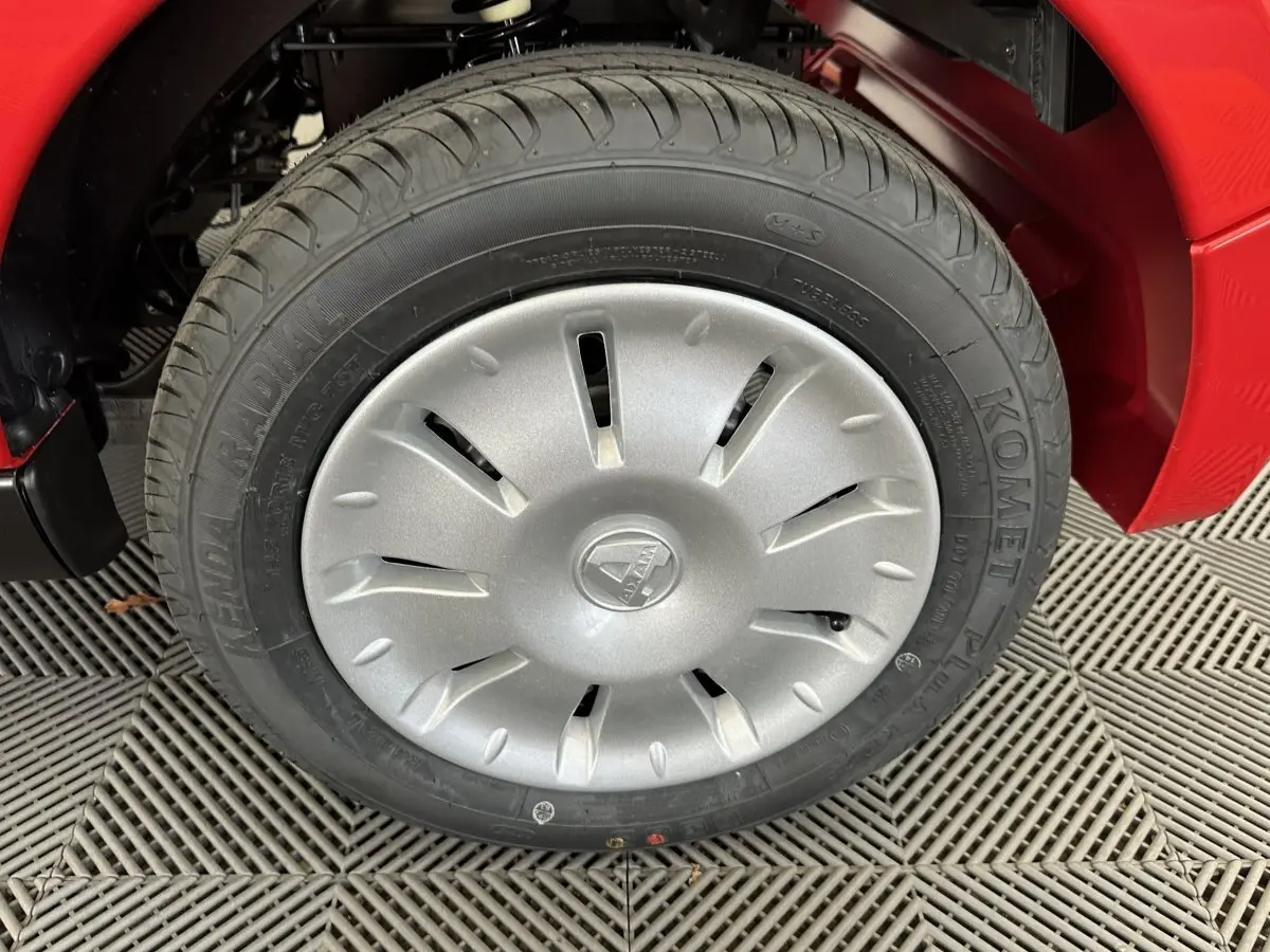 Gros plan sur la roue avant gauche d'une Aixam Ambition E City Pack rouge avec enjoliveur argenté au design aéré.