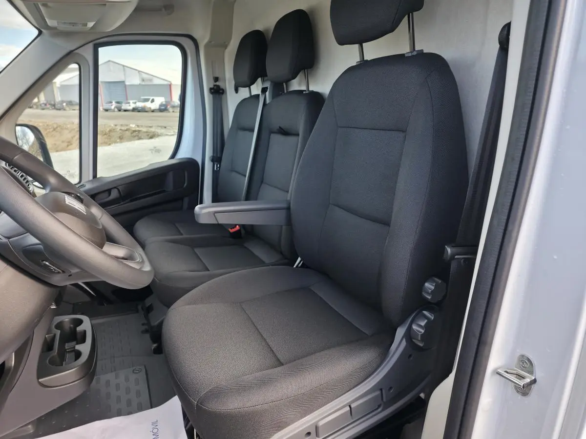 Vue intérieure côté conducteur du Fiat Ducato Fourgon blanc 2025, montrant les sièges tissu noir et le volant.