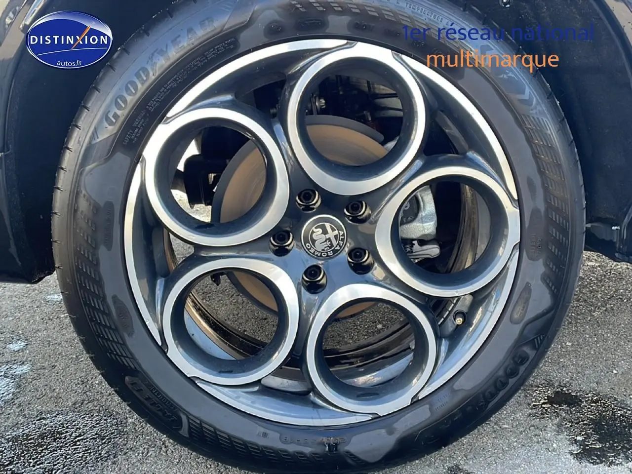 Gros plan sur la jante alu noire et argentée à cinq cercles de l'Alfa Romeo Tonale blanc, roue avant droite visible.