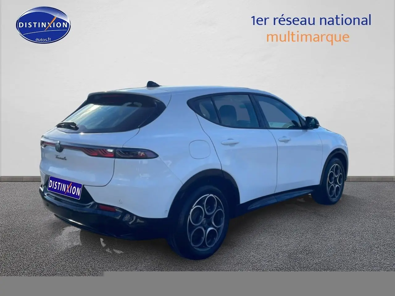 Vue 3/4 arrière droite d'un Alfa Romeo Tonale blanc avec jantes alu distinctives et feux arrière LED fins.