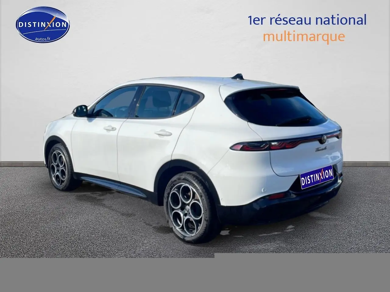 Vue 3/4 arrière droite d'une Alfa Romeo Tonale blanche avec jantes alu et feux arrière LED allumés.