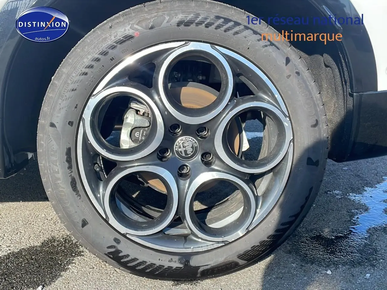 Gros plan sur la jante alu noire et argentée de l'Alfa Romeo Tonale blanche, roue avant droite visible.