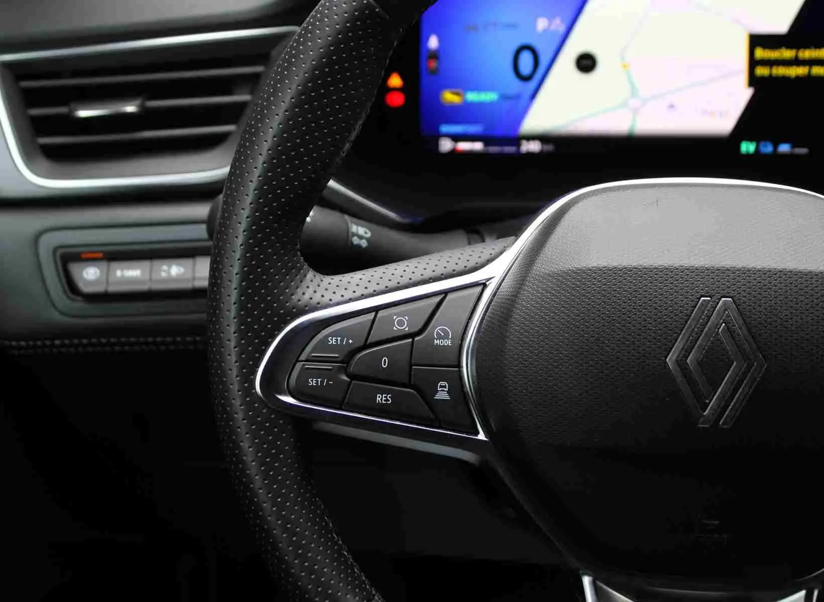 Gros plan sur le volant perforé noir du Renault Symbioz 2025 avec commandes intégrées et écran numérique en arrière-plan.