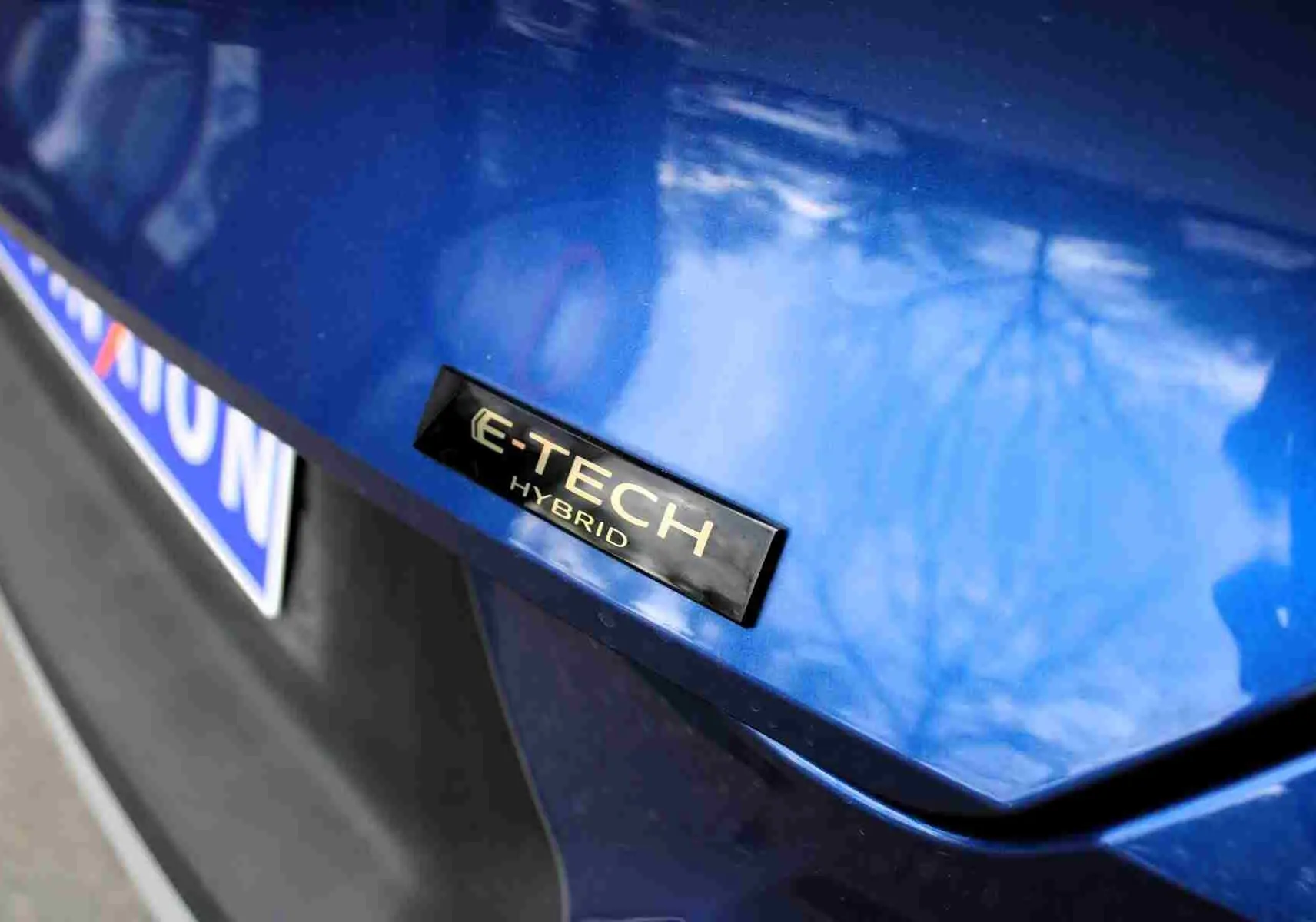 Gros plan sur l'arrière bleu iron metal d'une Renault Symbioz avec le badge E-TECH Hybrid visible.