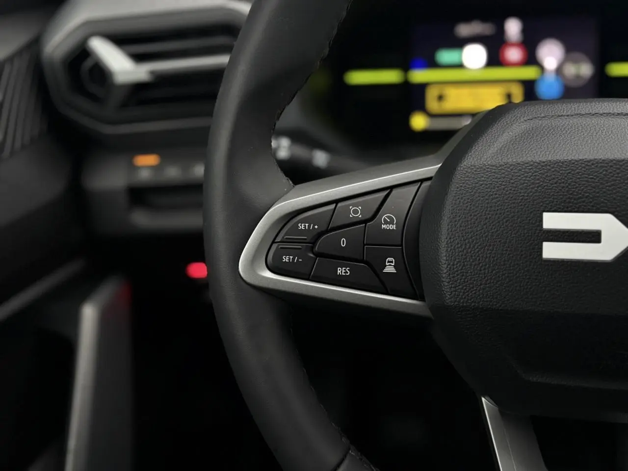 Gros plan sur le volant noir du Dacia Duster 2026 avec commandes intégrées et tableau de bord digital flou en arrière-plan.