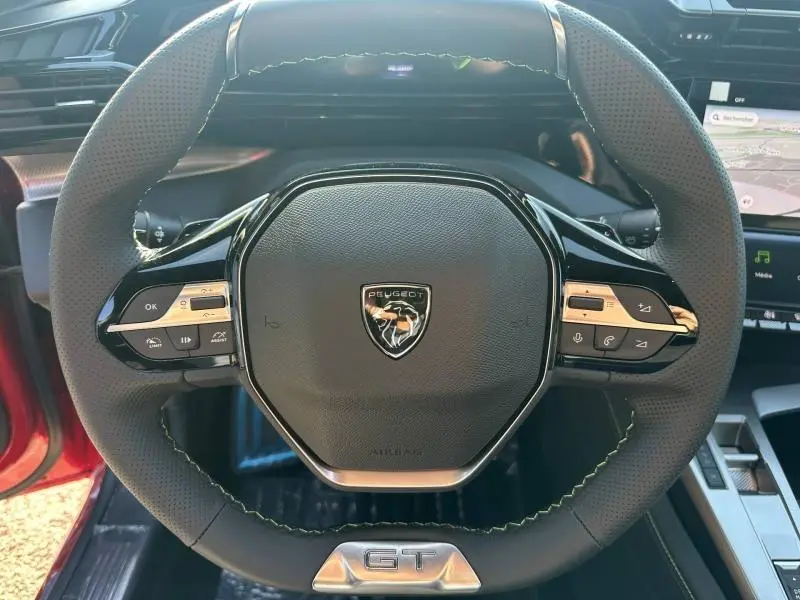 Vue rapprochée du volant multifonction noir avec logo Peugeot et badge GT d'une 308 Rouge Elixir 2025.