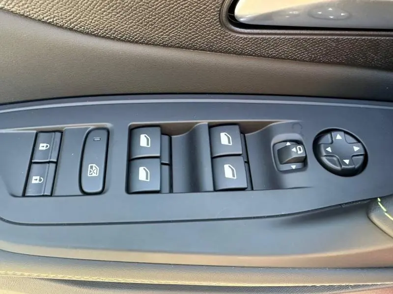 Gros plan sur les commandes des vitres et rétroviseurs côté gauche de la Peugeot 308 Rouge Elixir 2025.